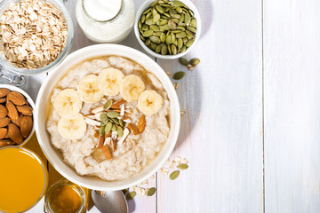 bowl of oatmeal with banana, honey and nuts on white background, top view