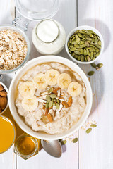 bowl of oatmeal with banana, honey and nuts on white background, vertical