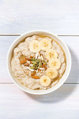 bowl of oatmeal with banana, honey and nuts on white table, vertical top view