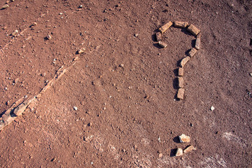 Un point d'interrogation dessiné à l'aide pierre sur un sol de terre ocre