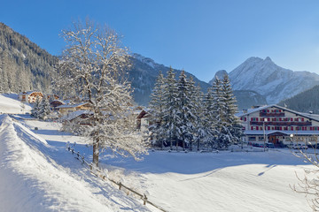 Snowy alpine village in Italy illuminated by sun with mountains in the background. Italian Dolomites, Trentino-Alto-Adige region, Italy