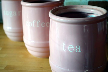 Three pink jugs on a wooden kitchen work surface, with the words Tea, Coffee and Sugar