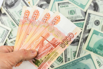 Hand holds Russian 5000 ruble banknotes on dollar bills background close-up