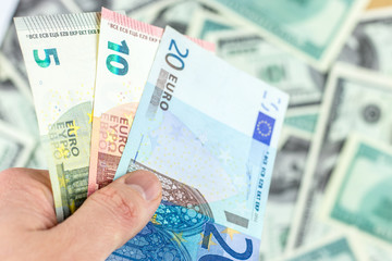 Hand holds 3 euro banknotes on dollar bills background close-up