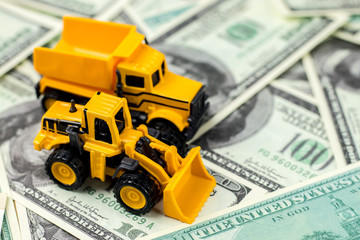 Fototapeta premium Construction vehicles for building concept. Yellow toys truck, backhoe on dollar bills background.
