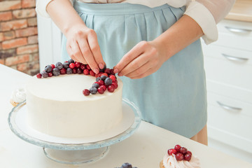 Women's hands decorated with red and blue berries white birthday cake