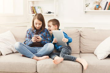 Two kids with gadgets on couch at home