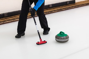 curling sport - player with broom sweeping the ice before stone