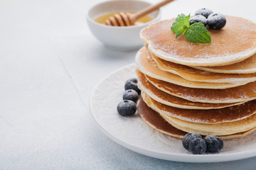 A stack of delicious pancakes with honey and blueberries on a light blue background. with copy space