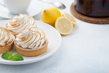 Lemon tartlets with meringue on vintage white plate and Cup of tea on the stone table. Tasty treat on a light blue background. With copy space