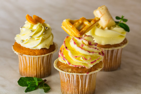Three cupcakes with different decorations on light background.