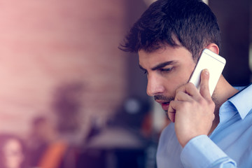 Portrait of a cheerful smiling men office worker talking on mobile phone while standing in modern...