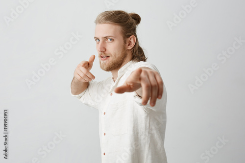 Confident Macho Man With Blond Hair And Bun Pointing At Camera