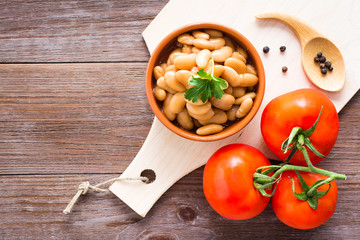 Cooked beans in tomato sauce in a bowl on the kitchen table. Fresh tomatoes and spices. Top view