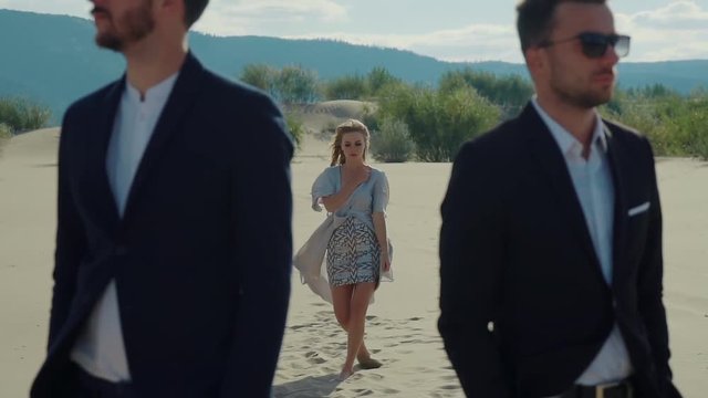 Beautiful woman in a dress coming from behind to two handsome men. She doesnt know who to choose.