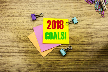 2018 goals on yellow sticky note, on wooden background. New Year resolutions concept.