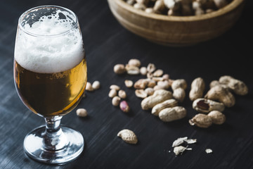 Glass of beer and peanuts on the wooden background