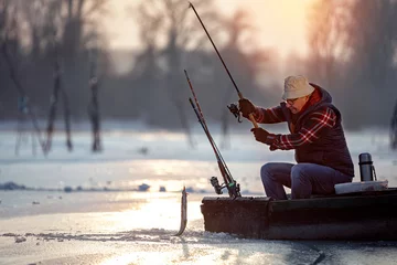 Foto auf Acrylglas Sport Fischer, der bei Sonnenaufgang auf Eis fischt