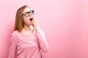 Young woman yawning on a solid background