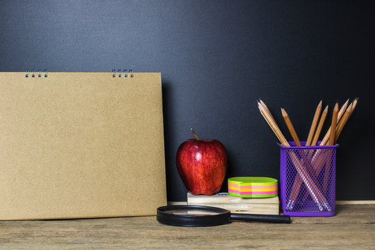 Red apple and stationery on wood table with Blackboard (Chalk Board) as background with copy space. Education and Back to school concept.