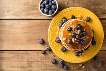 Pancakes with blueberries, walnuts and honey on wooden background.