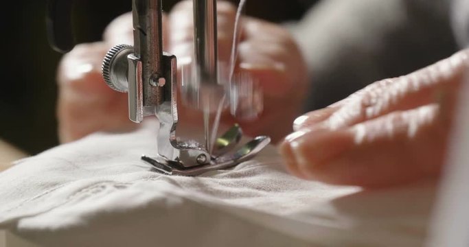 A hand of a young seamstress sewing a white cloth tailoring according to the tradition of tailors. The dressmaker uses perfectly needle and thread to sew traditional concept, sewing, style and fashion