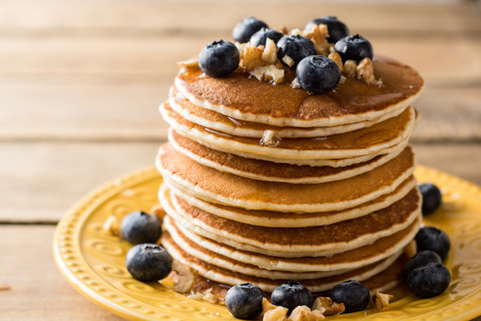 Pancakes with blueberries, walnuts and honey on wooden background.