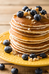 Pancakes with blueberries, walnuts and honey on wooden background.