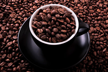 Black coffee cup and saucer one single for espresso or capuccino filled full of coffee beans on a background of scattered dark coffee beans photo 