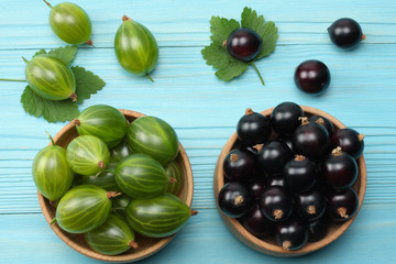 black currant in wooden bowl with gooseberry on blue wooden background. top view with copy space