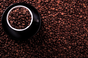Black coffee cup and saucer one single for espresso or capuccino filled full of coffee beans on a background of scattered dark coffee beans photo 