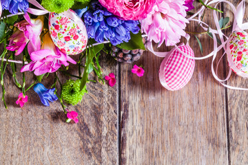 Girlande aus Frühlingsblumen und Textil-Ostereiern auf vintage-Holztisch mit viel Textfreiraum