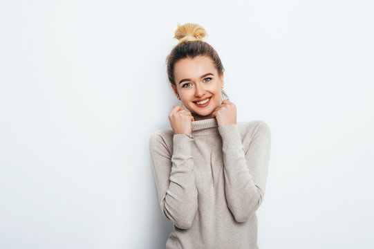 Portrait of cheerful good looking woman with appealing smile, having hair bun wearing in sweater isolated over white background. Beautiful female showing her pleasant emotions. People Beauty Fashion