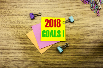 2018 goals on yellow sticky note, on wooden background. New Year resolutions concept.