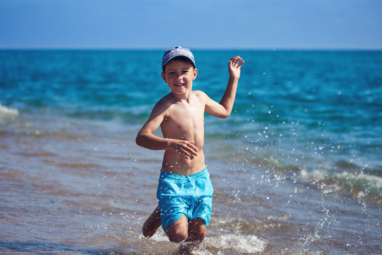 Smiling caucasian boy is running along the sea shore.