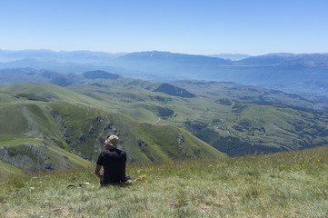 Fototapeta na wymiar man sitting on the grass looking at the mountains of the Apennines