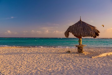 tropical Caribbean beach at sunset with straw umbrellas and white sand island of Aruba