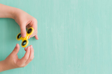 Child's hand spinning a fidget spinner device on turquoise background. Top view. Playing with a...