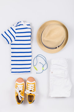 Child's striped t-shirt, demin shorts, accessories, yellow shoes and straw hat isolated on white background. Top view. Flat lay. Kid's summer clothes collage