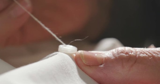 A hand of a young seamstress sewing a white cloth tailoring according to the tradition of tailors. The dressmaker uses perfectly needle and thread to sew traditional concept, sewing, style and fashion