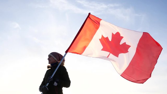 Young woman waving a flag of Canada against a blue sky. Fan Support of national team