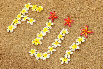 Fototapeta na wymiar Word Fiji written on a beach with plumeria flowers
