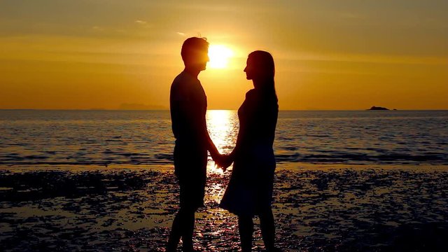 Couple silhouette staring at sunset on the beach start kissing and she lifts one leg up bending her knee in Koh Phangan island, Thailand. Valentine Day, honeymoon romantic love celebration concept