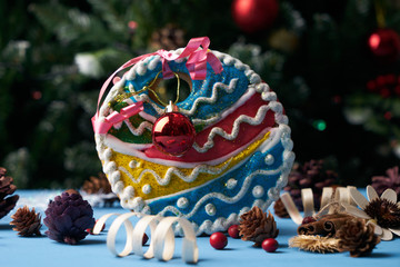 Homemade gingerbread ball cookie with festive decoration under the Christmas fir tree with garlands and colorful christmas tree bauble on background