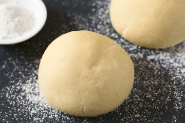 Ungebackener Hefeteig oder Germteig für die Zubereitung von Brot, Brötchen oder Pizza auf bemehlter Fläche, fotografiert mit natürlichem Licht (Selektiver Fokus, Fokus auf die Vorderseite des Teiges)
