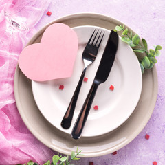 Table setting with a pink paper heart. White and grey plates, champagne glasse, cutlery and decorative textile on ultra violet background