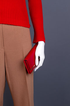 Female mannequin with red purse. Dummy dressed in women red sweater adn brown trousers, grey background.