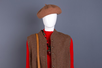 Mannequin dressed in beret and waistcoat. Red sweater, necklace and sleeveless vest for women. Women beauty and fashion.