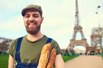 Handsome smiling bearded man holding baguette in hands over Eiffel Tower background. Paris, France