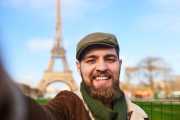 Handsome smiling bearded man taking a selfie over Eiffel Tower background. Paris, France